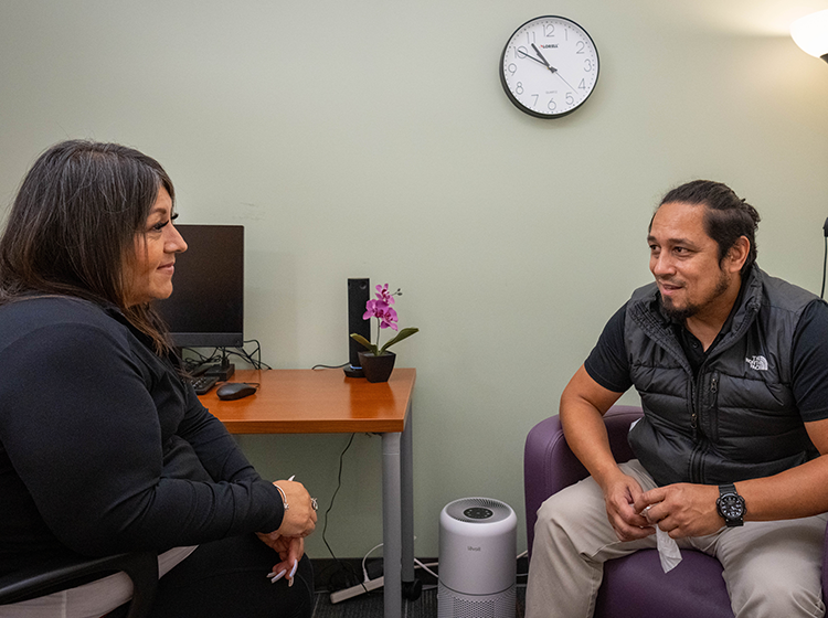 A Latinx young man speaks to a Native American woman therapist in a private room at the 爱妹社 Student Psychological Services.